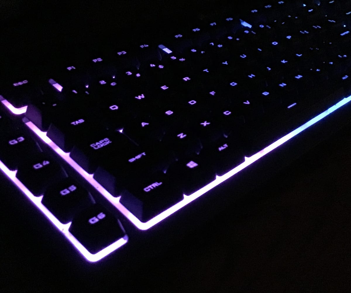 A full-size mechanical keyboard glowing purple and blue in a darkened room.